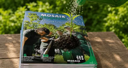 Stapel mit aktuellen Mosaik Magazinen, darauf wächst ein Pflänzchen, das mit einer grünen Gießkanne gegossen wird (Hinweis: KI-generiert)