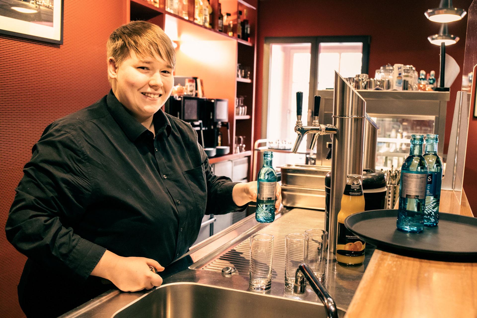 Eine Auszubildende in der Gastronomie bereitet Getränke hinter dem Tresen vor