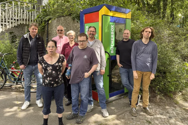 Gruppenfoto aller Beteiligten von Mosaik (BFB Ulmenallee) und der Ev. Kirchgemeinde vor der neu aufgestellten, bunt bemalten Bücherbox