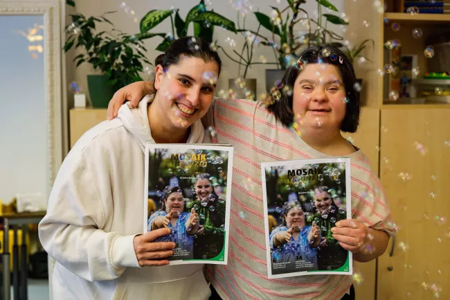 Zwei Beschäftigte der Mosaik-Werkstatt für Menschen mit Behinderungen halten das Mosaik Magazin hoch - Die Ausgabe ist zum 60.  Jubiläum von Mosaik erschienen