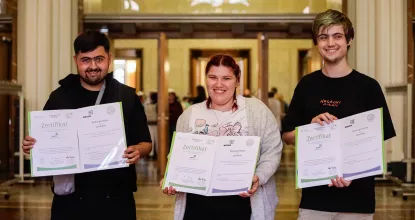 2 Absolventen und eine Absolventin von Mosaik halten stolz ihre Zertifikate im Roten Rathaus in die Kamera