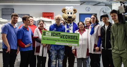 Auf dem Foto ist das Team aus der Wäscherei, zusammen mit Herthinho und 2 Hertha Spielern. Sie halten das Schild "Schichtwechsel" hoch.