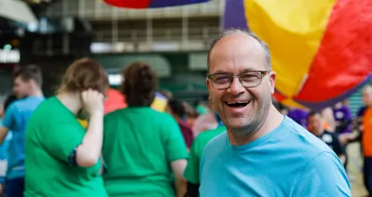 Mann schaut in die Kamera. Hinter ihm fliegen große, bunte Bälle