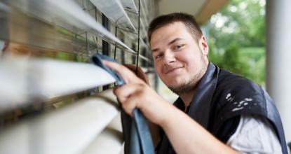 Eine  Mitarbeiter der Gebäudereinigung von Mosaik reinigt die Lamellen der Außenjalousie