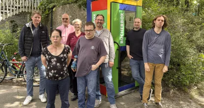 Gruppenfoto aller Beteiligten von Mosaik (BFB Ulmenallee) und der Ev. Kirchgemeinde vor der neu aufgestellten, bunt bemalten Bücherbox