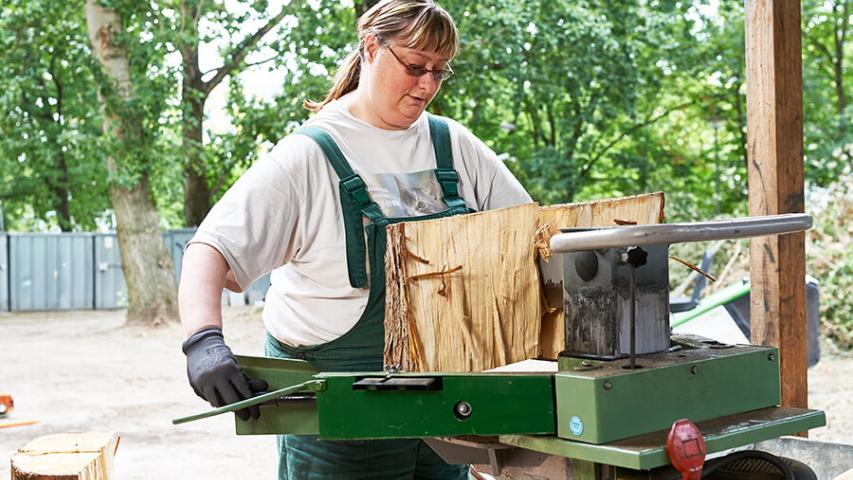Mitarbeiterin der Garten- und Landschaftspflege arbeitet an der Holzspaltmaschine