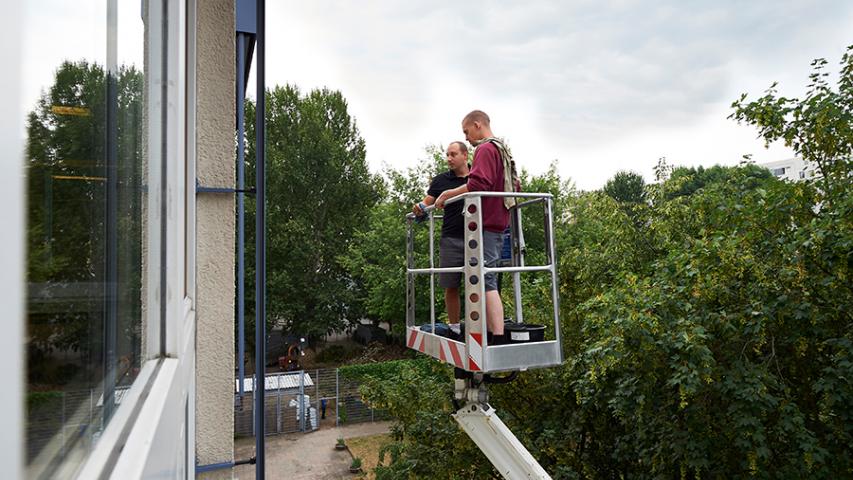 Gebäudereiniger-Gesellen von Mosaik-Services auf einem Steiger beim Reinigen der Außenjalousien