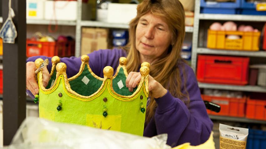 Mitarbeiterin fertigt einen grünen Kronenkorb in der Betriebsstätte Spandau