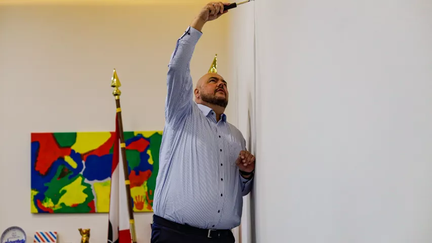 Frank Bewig greift selbst zum Schraubendreher - beim Anbringen des Werkes "Spandauer Allerlei" von Suzy van Zehlendorf in seinem Büro