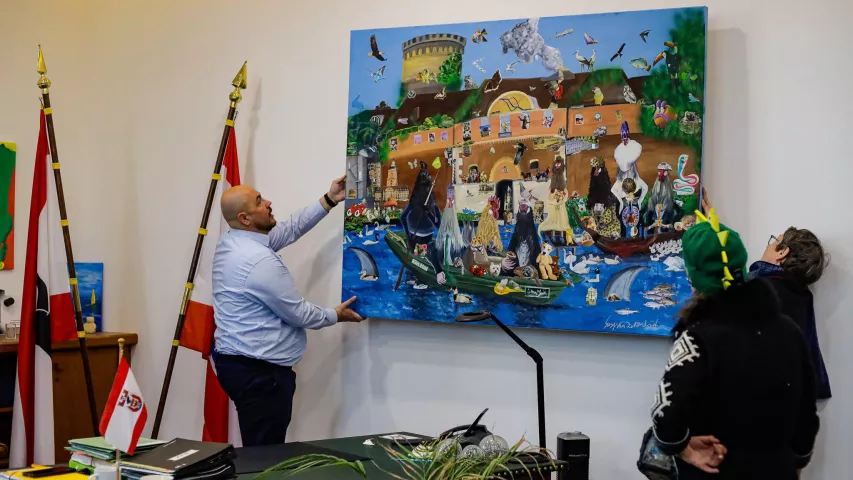 Frank Bewig und Nina Pfannenstiel, Leiterin der Kunstwerkstatt Mosaik Berlin, hängen das Bild "Spandauer Allerlei"