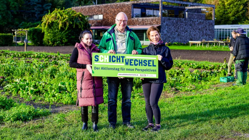 Schichtwechsel 2026 im Gärtnerhof Charlottenburg - 3 externe Gäste halten Schichtwechsel-Schild vor Salatfeld