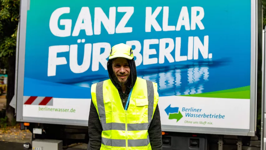 Schichtwechsel bei den Berliner Wasserbetrieben - Beschäftigter von Mosaik mit Helm und Warnweste vor Fahrzeug der Wasserbetriebe mit der Aufschrift "Ganz klar für Berlin"